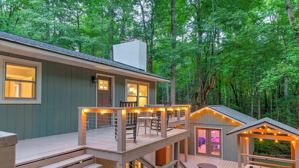 A two-story cabin with a deck, outdoor seating, and a hot tub.