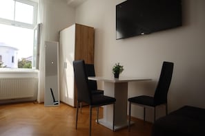 A modern room with a dining table, two chairs, a TV, and a view of a building outside.