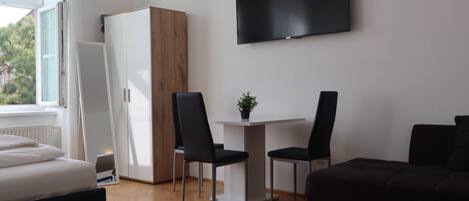 A modern room with a bed, a desk with two chairs, a TV, and a wardrobe.