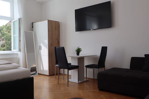 A modern room with a bed, a desk with two chairs, a TV, and a wardrobe.