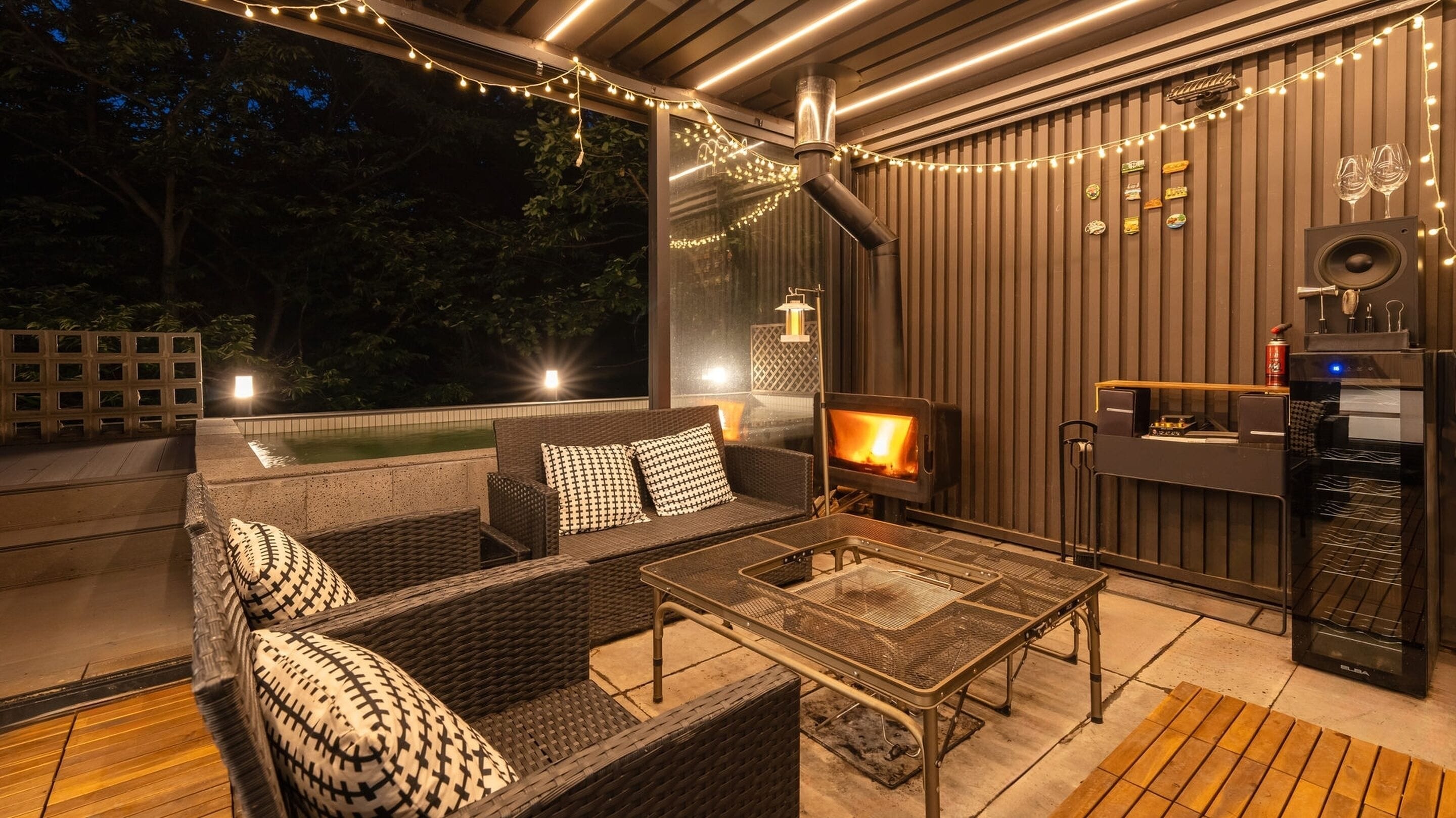 A cozy outdoor seating area with wicker furniture, a glass table, and a wood-burning stove.