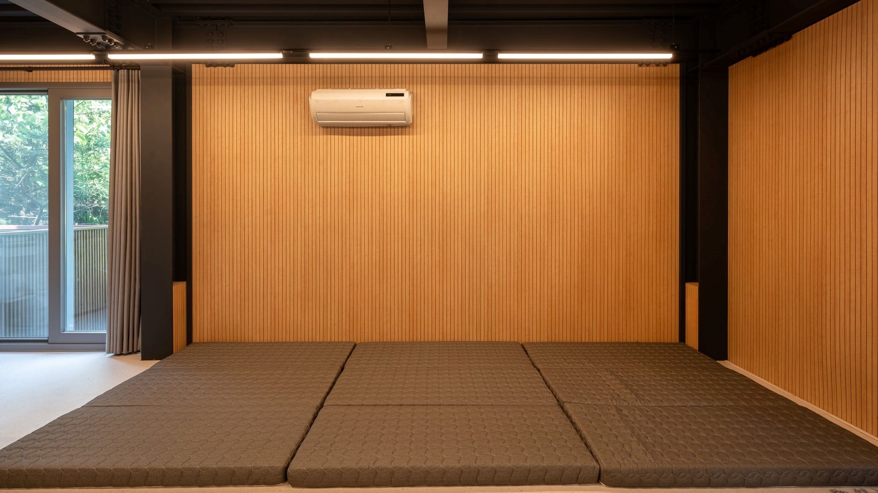 Una habitación con pared de paneles de madera, aire acondicionado instalado en el techo y una plataforma baja con superficie texturizada.