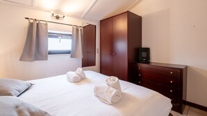 A hotel room with a large bed, a wooden wardrobe, a desk with a computer, and a window with curtains. - Reynaertpark with parking by Interhome (Bredene)