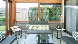 A sunlit patio with a glass table, metal chairs, and a bench with patterned cushions. - Reynaertpark with parking by Interhome (Bredene)
