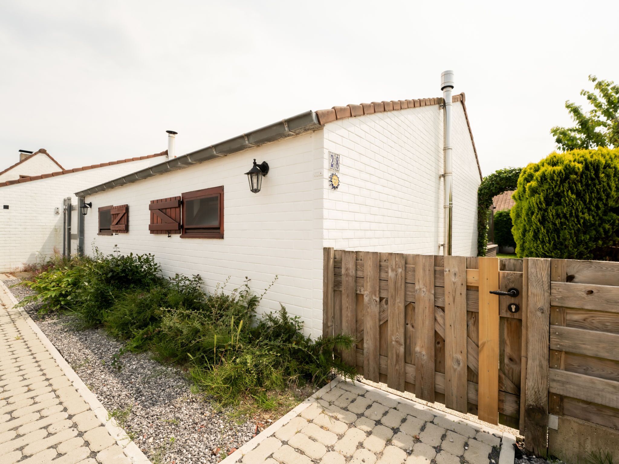 A white building with a wooden fence, a paved pathway, and green shrubs.