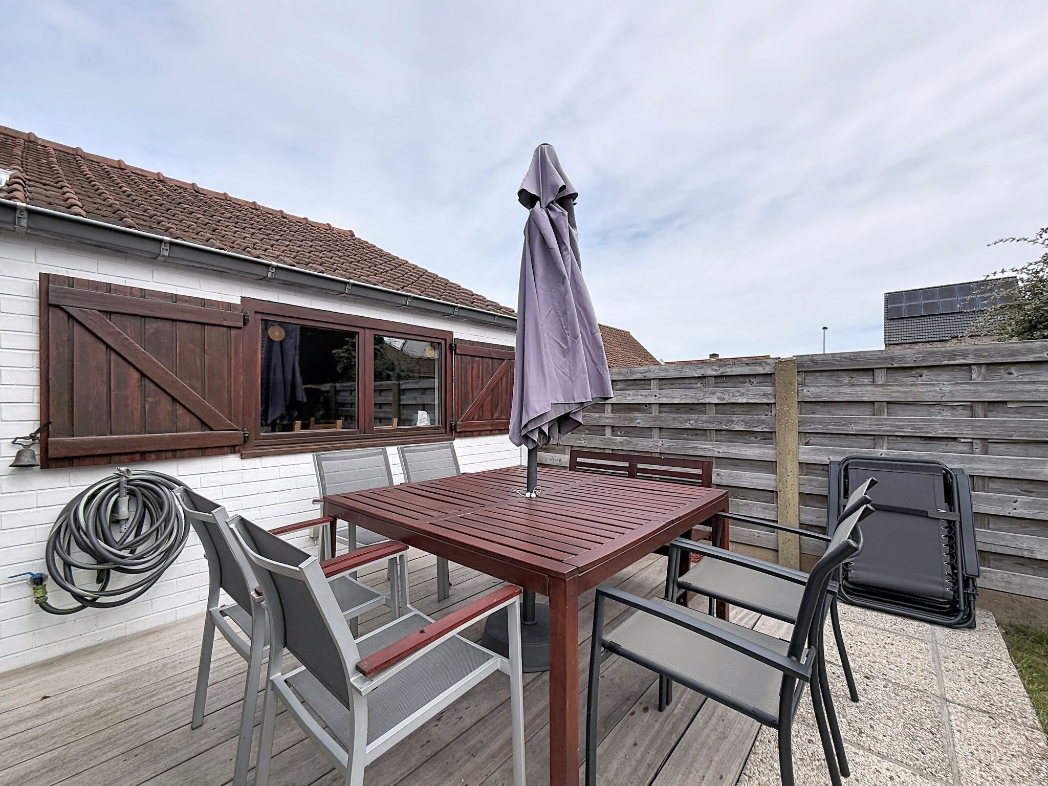 A patio with a table and chairs, a wooden fence, and a house with shutters.