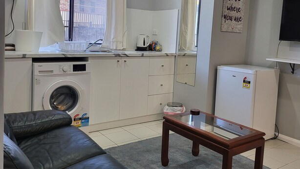 Een compacte woonruimte met een wasmachine, een kleine koelkast, een bank en een bijzettafeltje.