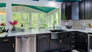 Una cucina moderna con mobili scuri, una lavastoviglie in acciaio inossidabile e un'ampia finestra che offre vista sul verde.