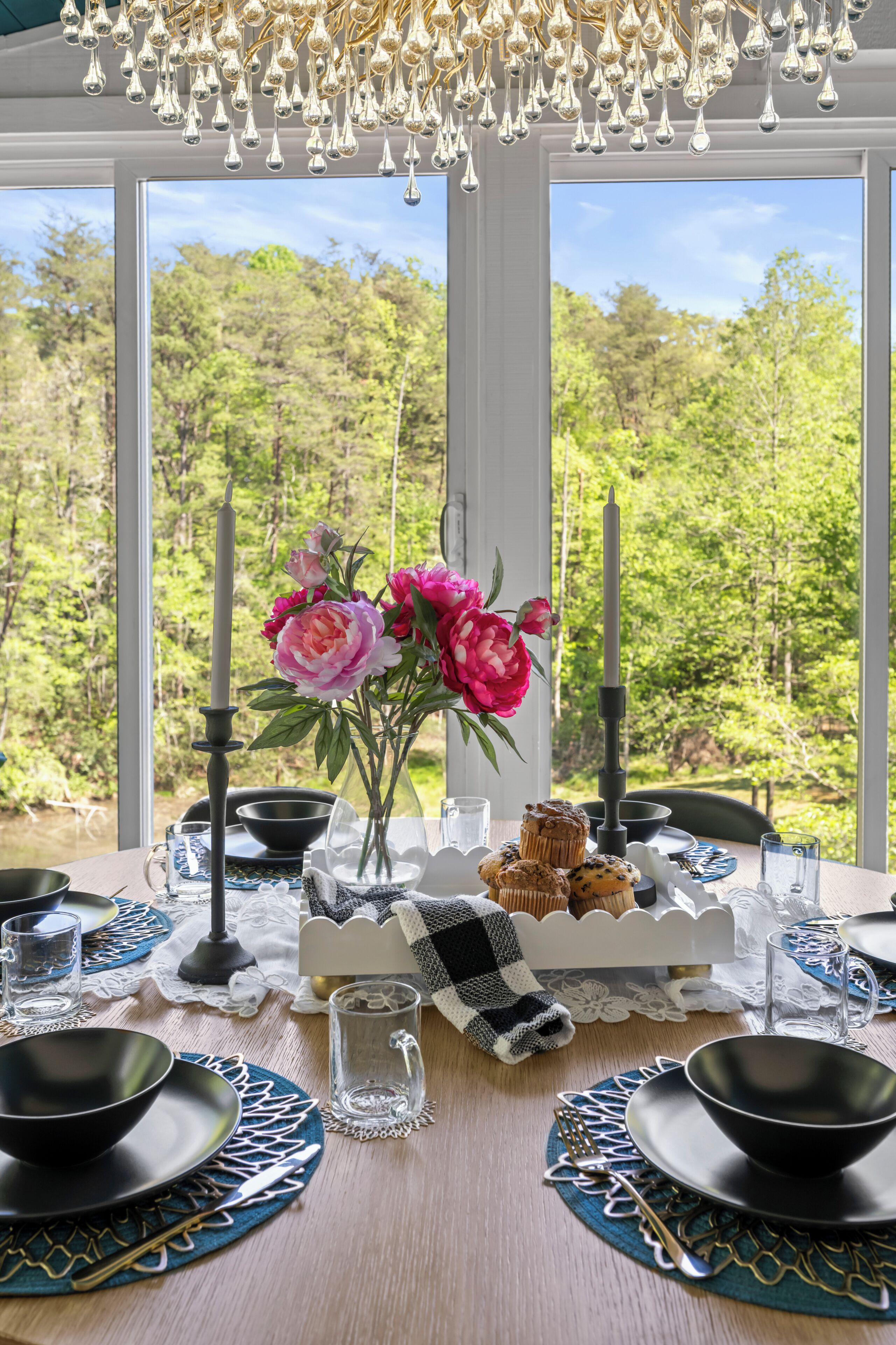 Una mesa de comedor dispuesta con cuencos, platos y cubiertos negros, un florero con flores y un candelabro.
