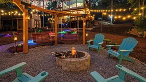 Un giardino sul retro con un braciere, altalene, poltrone Adirondack e luci decorative appese.