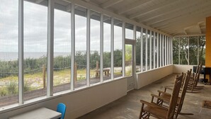 A room with large windows, a concrete floor, and wooden rocking chairs. - SATSUMA SUNSET☀️ Spacious '70s beach bungalow 🏖️ beachfront 🌊 tranquil retreat (Alligator Point)