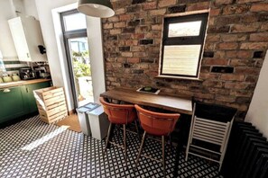 Compact kitchen with a brick wall, window, and geometric tile floor, featuring a counter with stools and a door to an outdoor area.