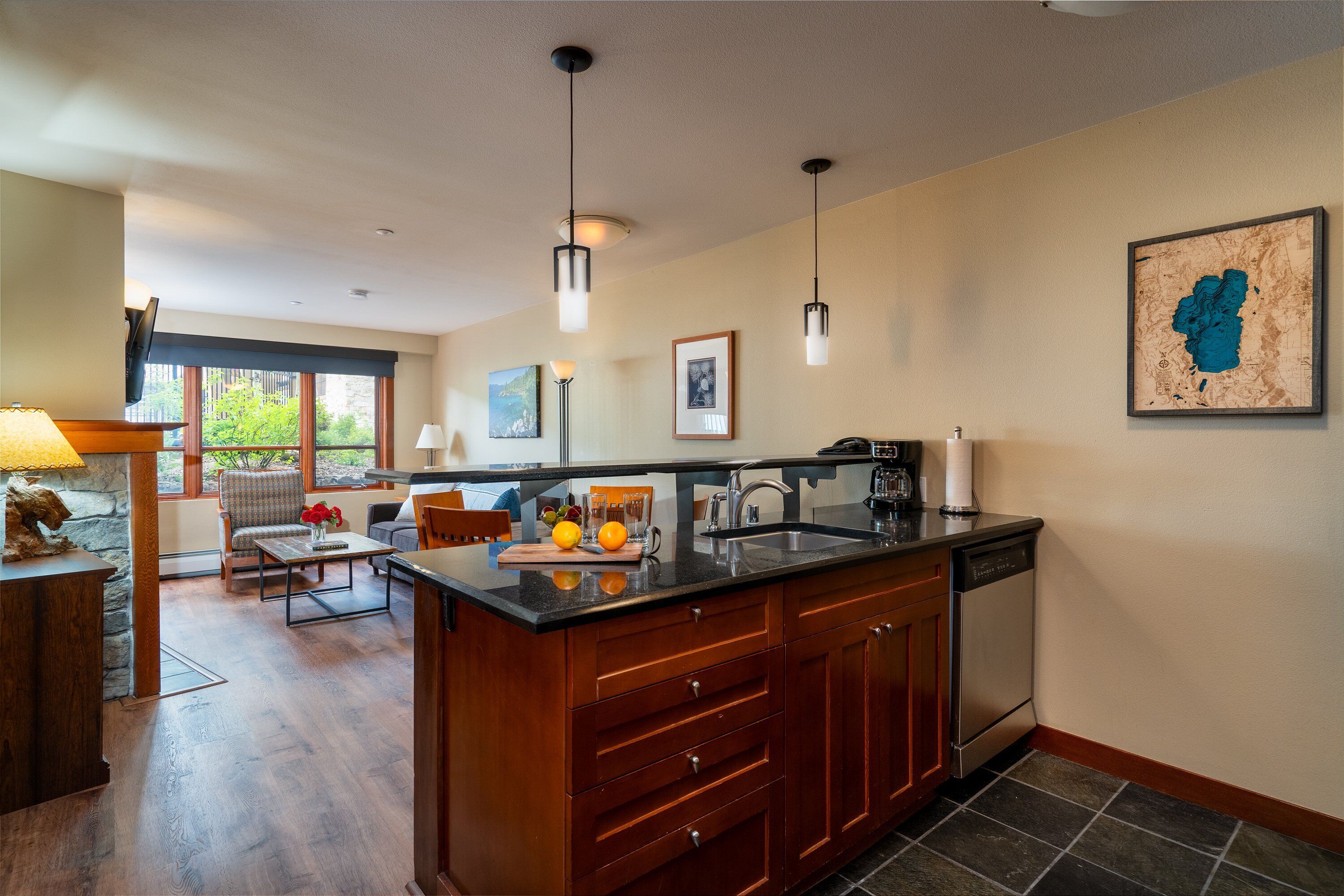 A modern kitchen with a large island, wooden cabinets, and a stone backsplash. There is a dining area with a table and chairs, and a large window providing natural light.