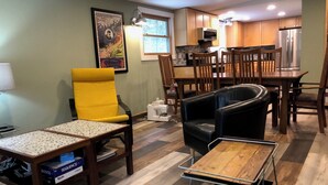 A modern living room with a yellow armchair, a black leather sofa, and a green couch. There is a wooden coffee table, a dining table with chairs, and a kitchen area with wooden cabinets and a stainless steel refrigerator. - Fresh, nicely finished, three-bedroom cabin on the Baileys Trails!  (Millfield)