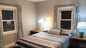 A bedroom with a bed, bedside tables, a lamp, and curtains. - Fresh, nicely finished, three-bedroom cabin on the Baileys Trails!  (Millfield)