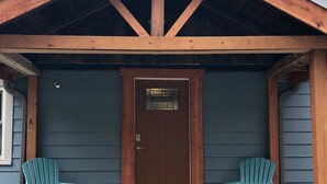A wooden cabin with a brown door, two turquoise Adirondack chairs, and a wooden bench in front. - Fresh, nicely finished, three-bedroom cabin on the Baileys Trails!  (Millfield)