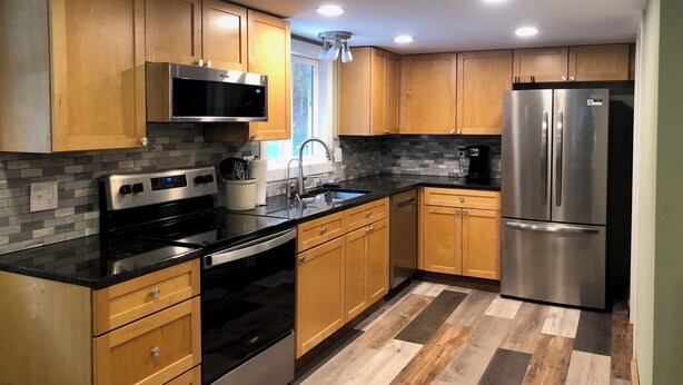 A modern kitchen with wooden cabinets, stainless steel appliances, and a black countertop. - Fresh, nicely finished, three-bedroom cabin on the Baileys Trails!  (Millfield)