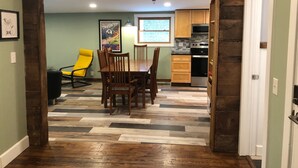 A dining area with a wooden table and chairs, a yellow chair, and a kitchen in the background with wooden cabinets and appliances. - Fresh, nicely finished, three-bedroom cabin on the Baileys Trails!  (Millfield)
