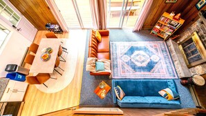 Un salón amplio con techo de madera, un sofá azul, un sofá de cuero marrón y una alfombra grande.