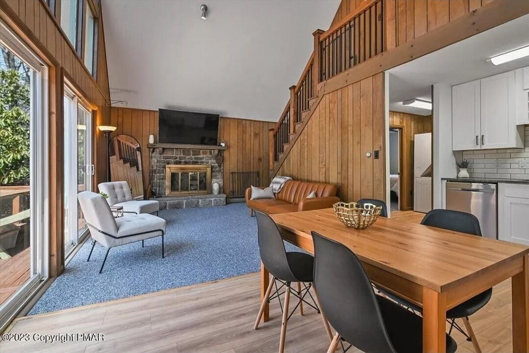 A spacious living area with a fireplace, a dining table, and a staircase leading to an upper level.