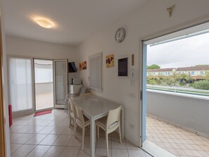 Une pièce comprenant une table à manger, des chaises, une horloge et une porte-fenêtre coulissante donnant sur un balcon.