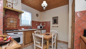 Una cocina con armarios de madera, estufa, microondas y una mesa de comedor con sillas.