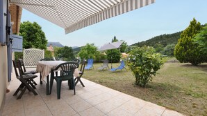 Un patio exterior con una mesa y sillas, una pérgola que proporciona sombra y vistas del paisaje circundante.