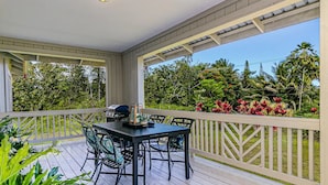 Une terrasse extérieure couverte, dotée d’une table et de chaises, entourée d’une balustrade blanche et d’une végétation luxuriante.