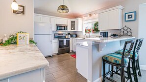 Une cuisine moderne avec des meubles blancs, un îlot central et un coin bar avec des tabourets.
