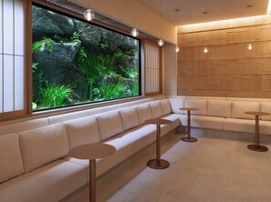 Relax in a serene outdoor setting with a view of lush greenery from the large window, and unwind on the comfortable bench or at one of the small tables.