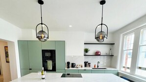 A modern kitchen with a large island, black bar stools, and pendant lighting. - Newly Refurbished w/ River Views (Greater London)
