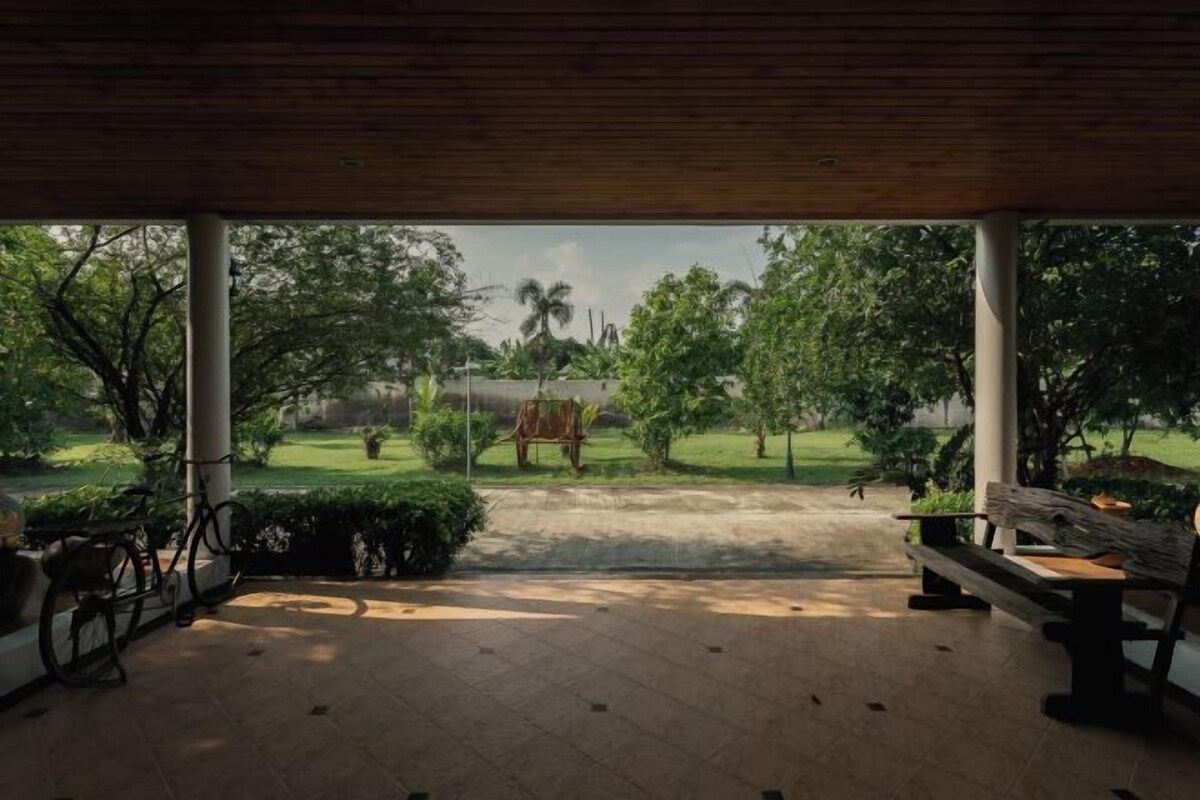 A covered outdoor area with a bench and a bicycle, overlooking a well-maintained garden with trees and a pathway.