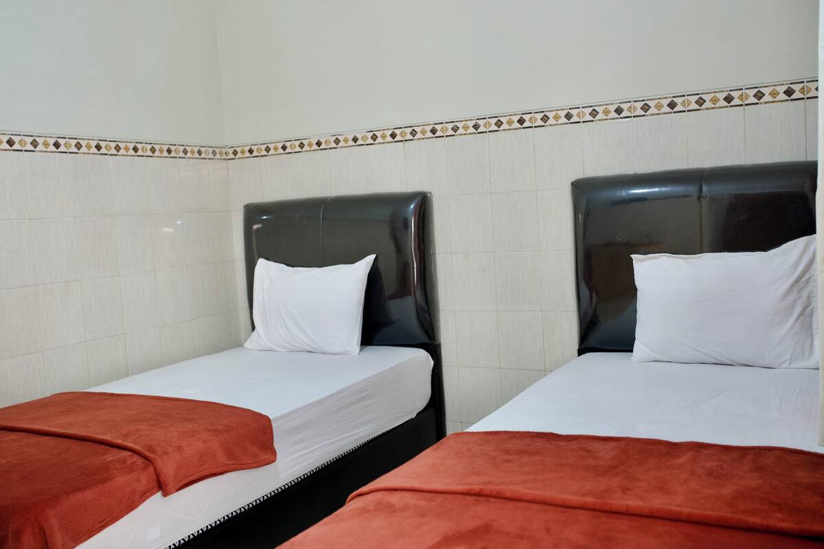 Two single beds with black headboards and white bedding, arranged in a small room with tiled walls and a decorative border.