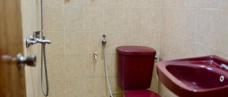 A bathroom with beige tiled walls, a red toilet, a red sink, and a shower with a handheld showerhead.