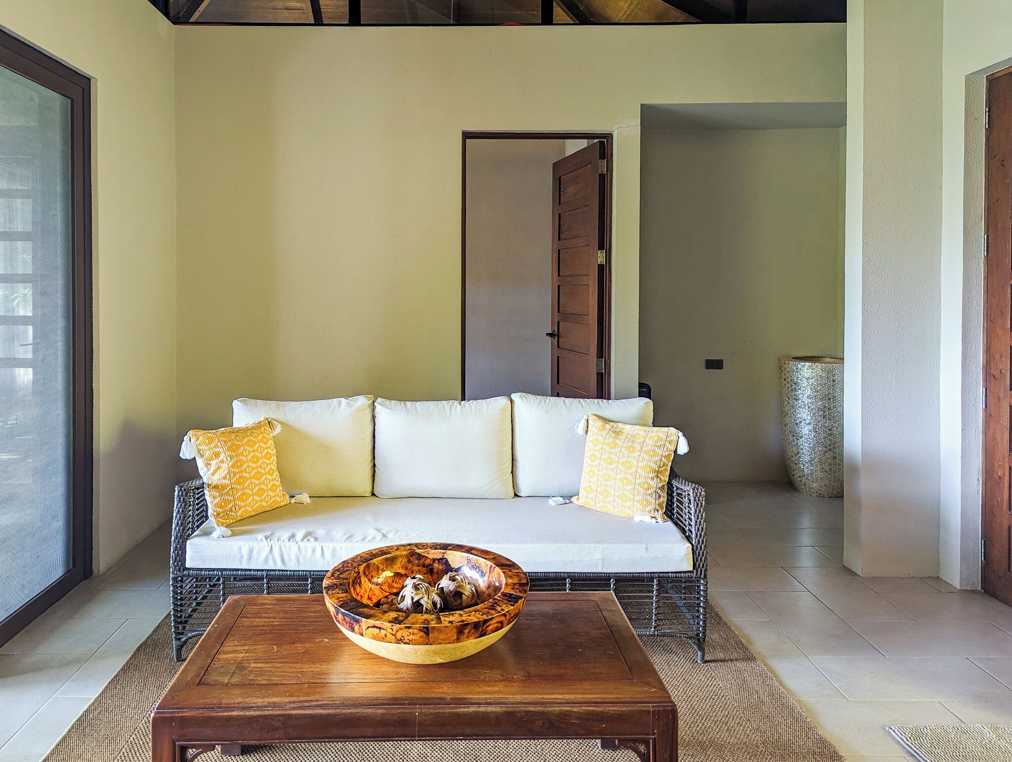 Una stanza con un divano bianco, due cuscini gialli decorati e un tavolino in legno con una ciotola decorativa.