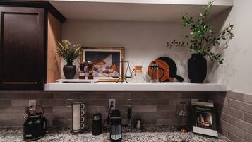 Een keuken met een granieten aanrecht, een koffiezetapparaat, een waterkoker en een lijst met een afbeelding aan de muur.