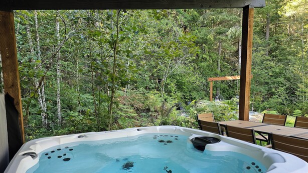 Un bain à remous situé dans un espace boisé, avec une terrasse en bois et des chaises.