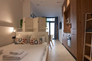 Une chambre moderne avec un lit, des oreillers, une table de chevet et une commode. On y trouve une armoire en bois et une petite plante accrochée au mur.