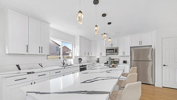 Una cocina moderna con armarios blancos, una isla grande e iluminación colgante.