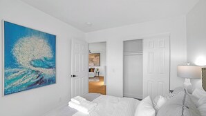 Un dormitorio con cama, mesita de noche, lámpara y un cuadro en la pared.