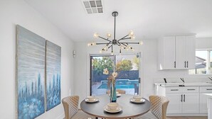 Una cocina moderna con armarios blancos, un comedor con una mesa redonda y sillas acolchadas, y un cuadro abstracto de gran tamaño en la pared.