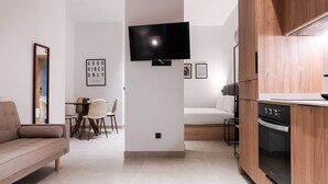A modern living room with a sofa, a dining area with chairs, a flat-screen TV mounted on the wall, and a kitchen with wooden cabinets and an oven. - VLC HOST - Zapadores I (Valencia)