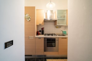 A compact kitchen with a gas stove, oven, and a hanging light fixture.