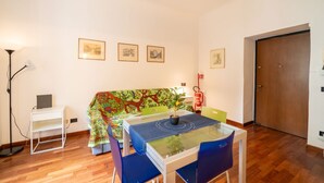 A room with a dining table, chairs, a sofa with a colorful blanket, a small white side table, a floor lamp, and a door. - Welcome to our exclusive residence in the heart of Milan, located in Porta Venezia, one of the liveliest and most sought-after areas of the city. This charming B&B offers you the perfect balance between modern comfort and Milanese authenticity.The apartm (Milano)