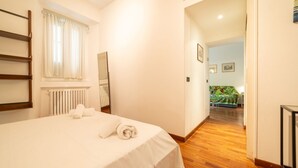 A bedroom with a bed, a radiator, a window with curtains, a wooden floor, and a hallway leading to another room. - Welcome to our exclusive residence in the heart of Milan, located in Porta Venezia, one of the liveliest and most sought-after areas of the city. This charming B&B offers you the perfect balance between modern comfort and Milanese authenticity.The apartm (Milano)
