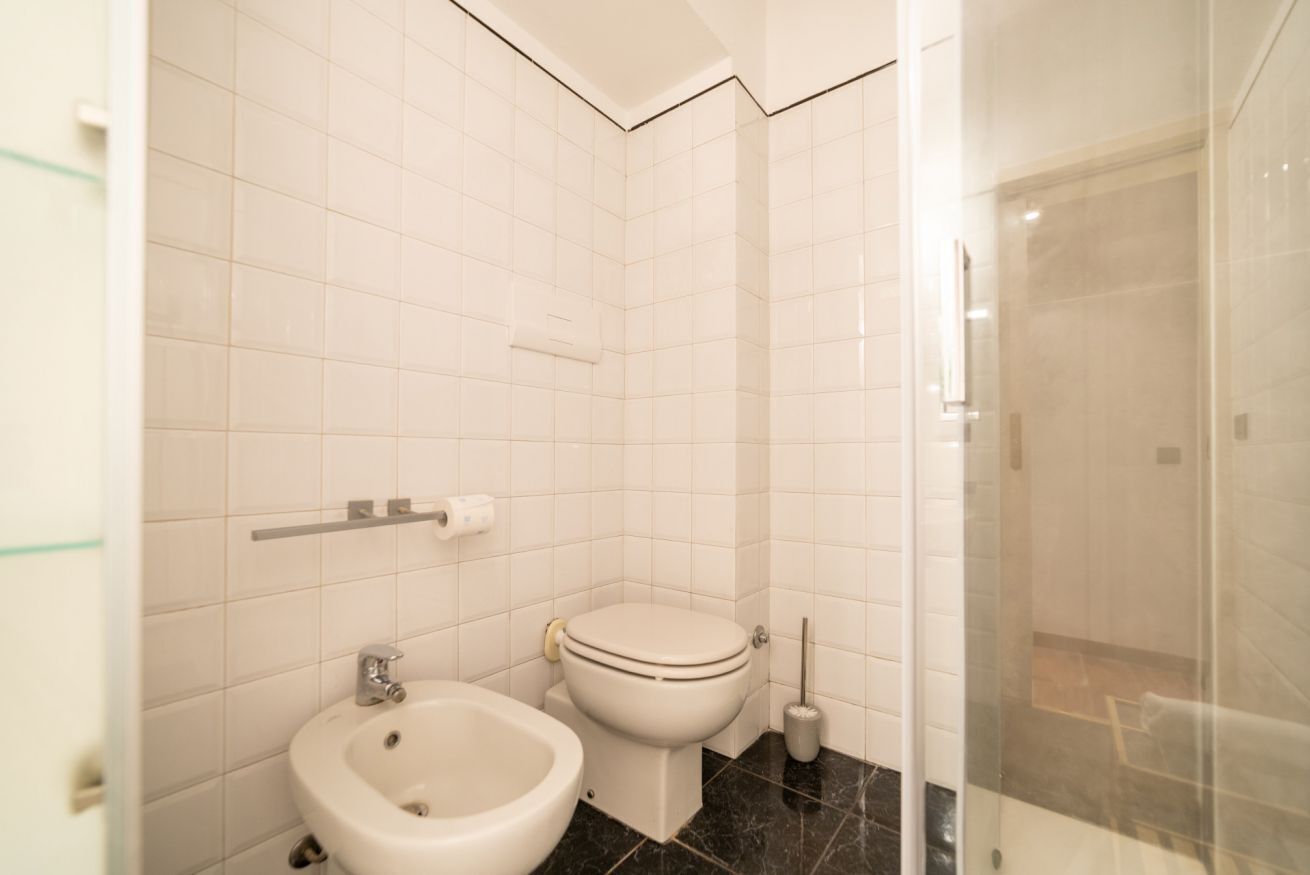 Een badkamer met witte tegels, een toilet, een douchecabine van glas en een bidet.