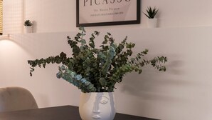 A white vase with a face design on a table, a framed Picasso portrait, and small potted plants on the wall. - VLC HOST - Zapadores E (Valencia)