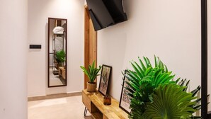 A hallway with a wooden bench, a mounted TV, a mirror, and potted plants. - VLC HOST - Zapadores E (Valencia)