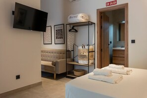 A hotel room with a bed, a sofa, a TV, a wardrobe, and a sign indicating the exit. - VLC HOST - Zapadores D (Valencia)
