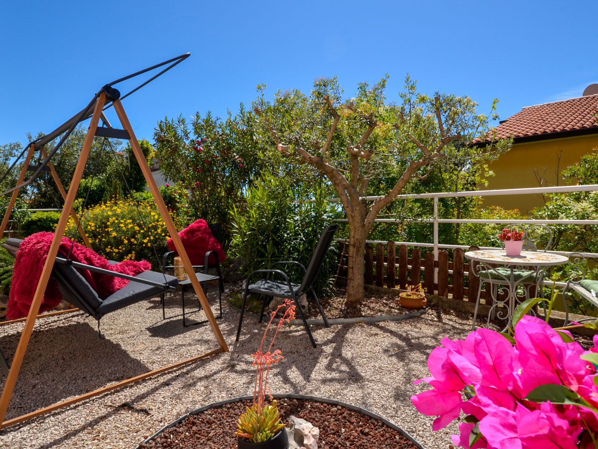 A patio with a swing set, outdoor seating, and a garden area with various plants and flowers.